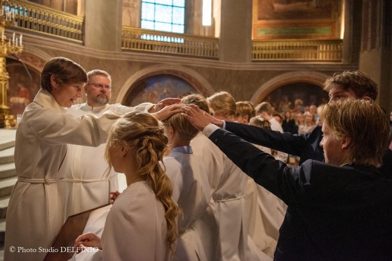 Alttarilla siunaus eli konfirmointi menossa. Pappi ja isoset laittavat kädet nuoren pään päälle.