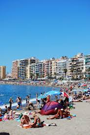 Fuengirola - suomalaisten paratiisi Espanjassa: korkeita kerrostaloja, rantaviivalla ihmisiä auringonotossa ja uimassa turkoosinvärisessä vedessä.